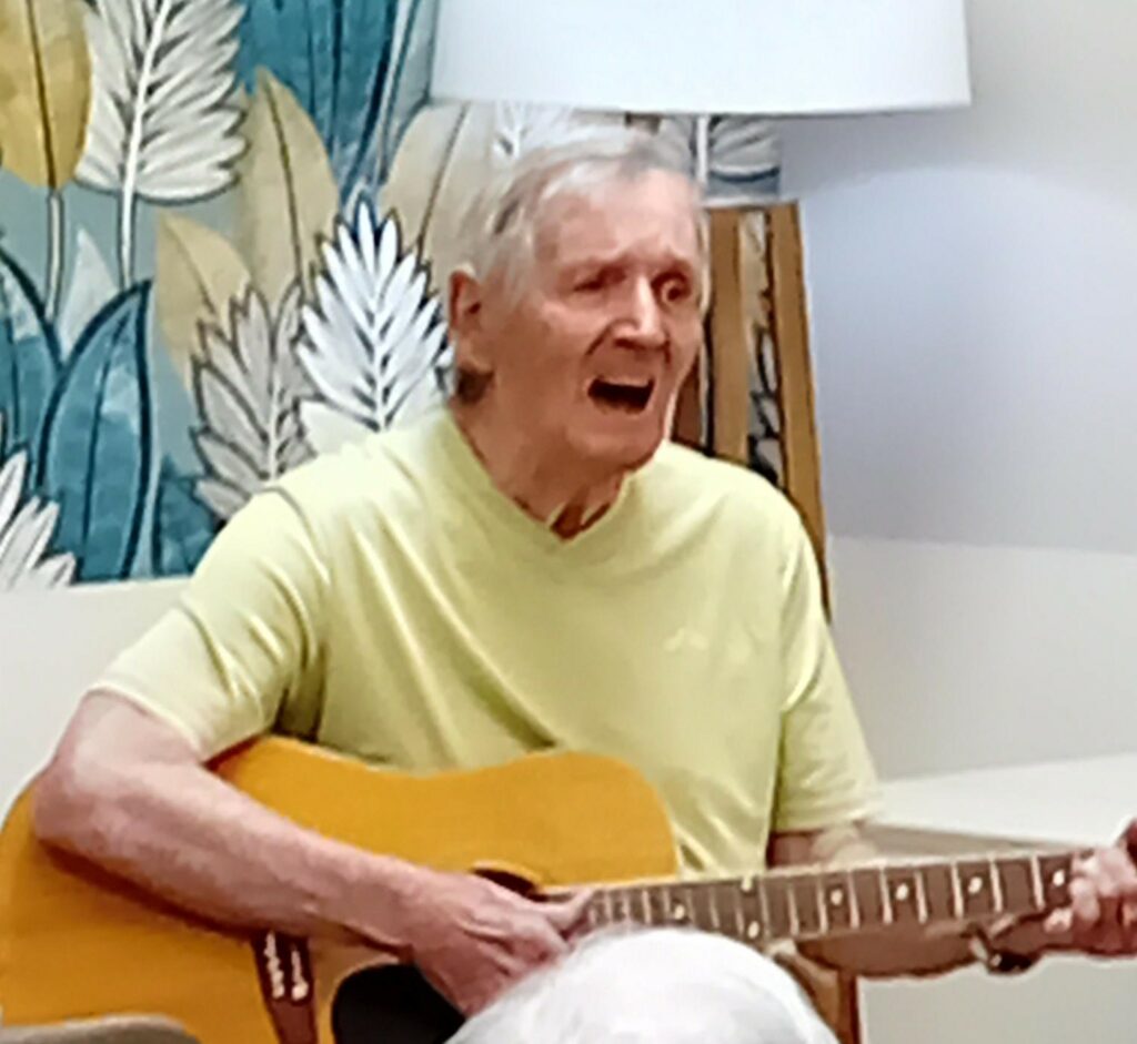 Musicien bénévole jouant de la guitare dans le salon de la résidence.